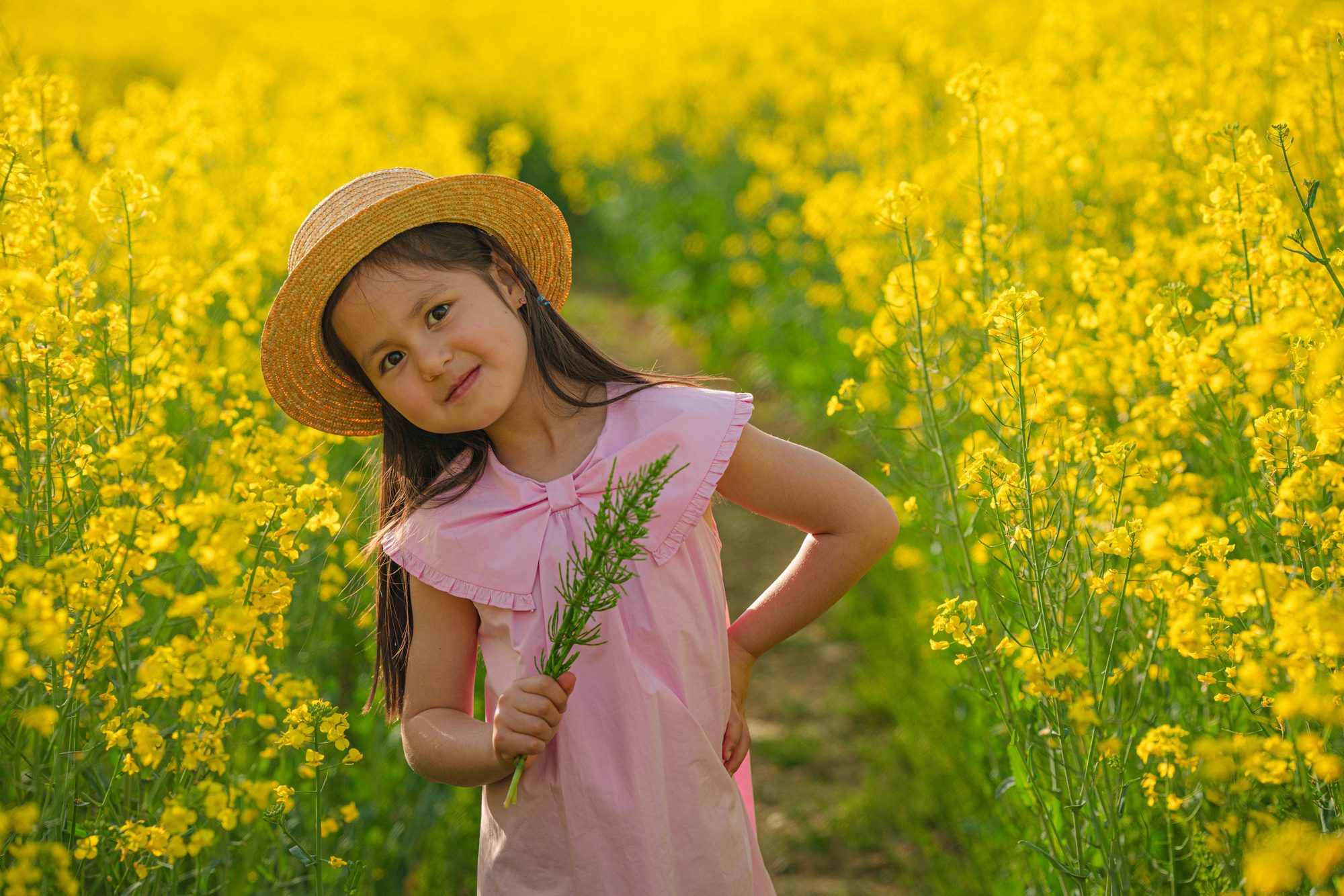 Enfant espiègle en robe rose dans le colza, main sur la hanche